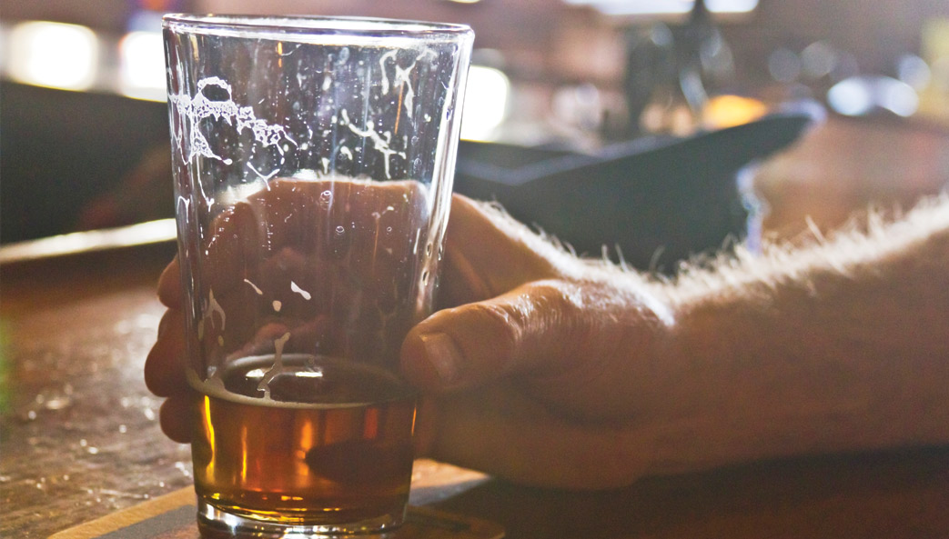 closeup of man's hand holding a beer glass that is almost empty