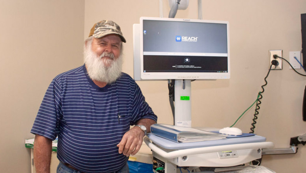 Dennis Hall stands next to the Remote Evaluation for Acute Ischemic Stroke (REACH) telemedicine cart that played a role in saving his life during an emergency visit to Emanuel Medical Center in Swainsboro, Ga. in November 2018. (Photo by Rebecca Ayer)