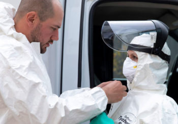 National EMS paramedic Blake Stewart helps fellow paramedic Kelly Glover suit up for treating an Ebola patient during an Ebola Transportation Exercise at the Institute for Disaster Management on the Health Sciences Campus.