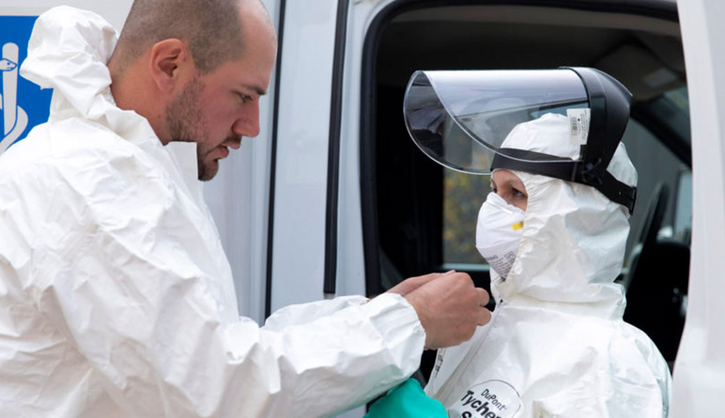 National EMS paramedic Blake Stewart helps fellow paramedic Kelly Glover suit up for treating an Ebola patient during an Ebola Transportation Exercise at the Institute for Disaster Management on the Health Sciences Campus.