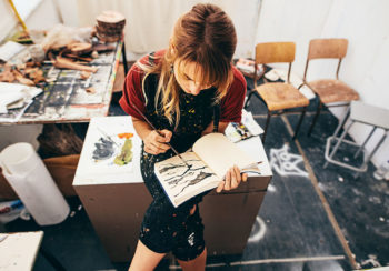 Young woman painting in her drawing book in a studio