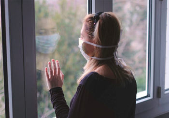 image of woman looking out the window wearing a face mask