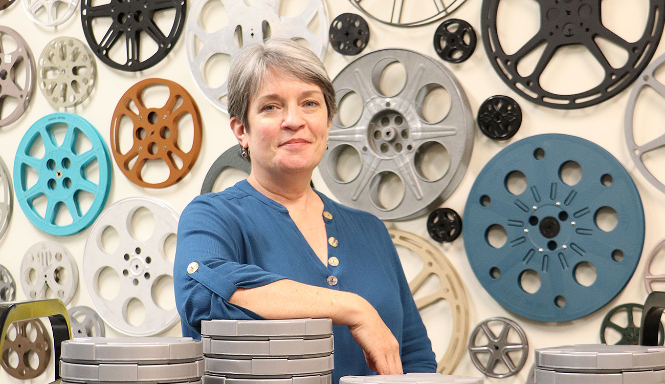 Margie Compton in front of wall covered in empty film reels