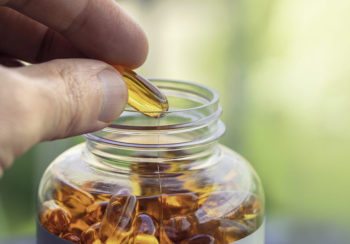 fingers holding fish oil capsule above bottle