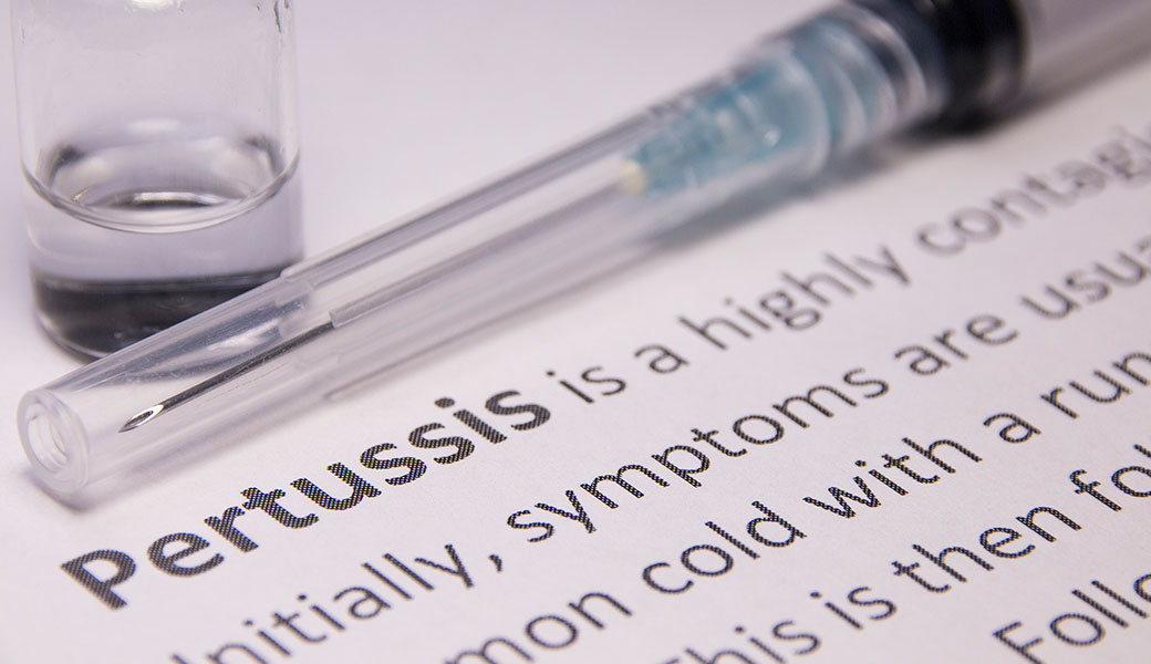 photo of a syringe lying on top of the definition of Pertussis