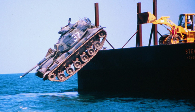 A battle tank is pushed into the ocean to form part of an artificial reef.