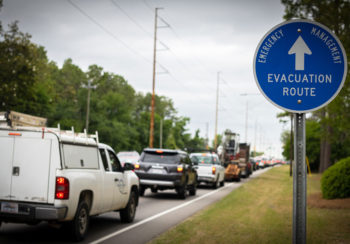 traffic lined up on street with sign for evacuation route next to road