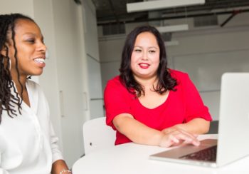 two working woman talking in front of laptop