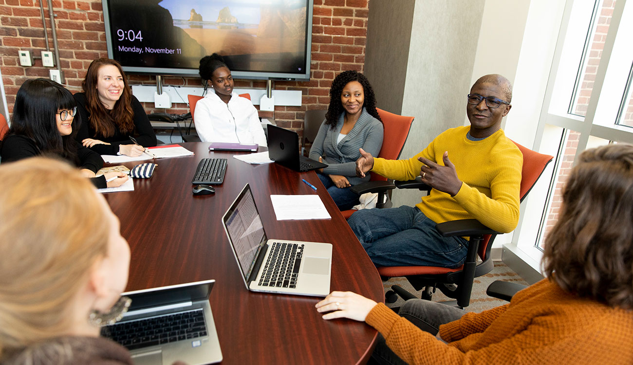 Social work professor David Okech, right, talks with a group of students in the conference room