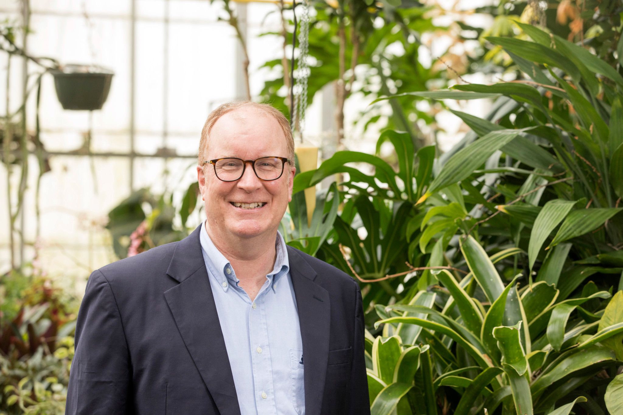 Man with glasses smiling in front of fern plants