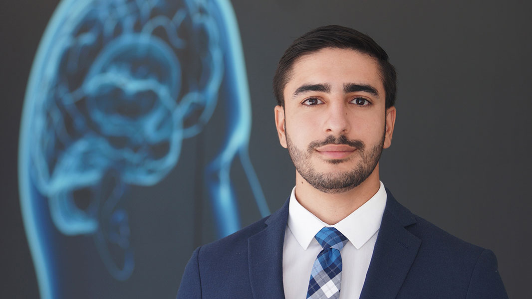 Man in business suit and tie standing in front of a 3D view of the brain.