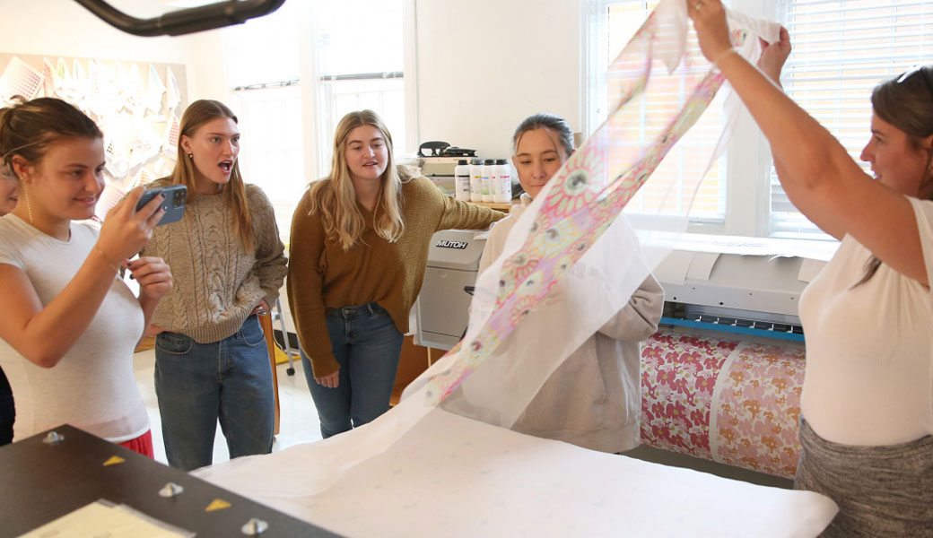 Fashion merchandising student showing a roll of fabric to other students.