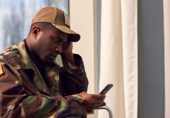 Injured American Soldier Wearing Uniform Sitting in Wheelchair Looking at Mobile Phone