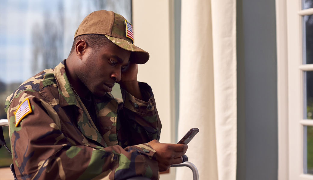 Injured American Soldier Wearing Uniform Sitting in Wheelchair Looking at Mobile Phone