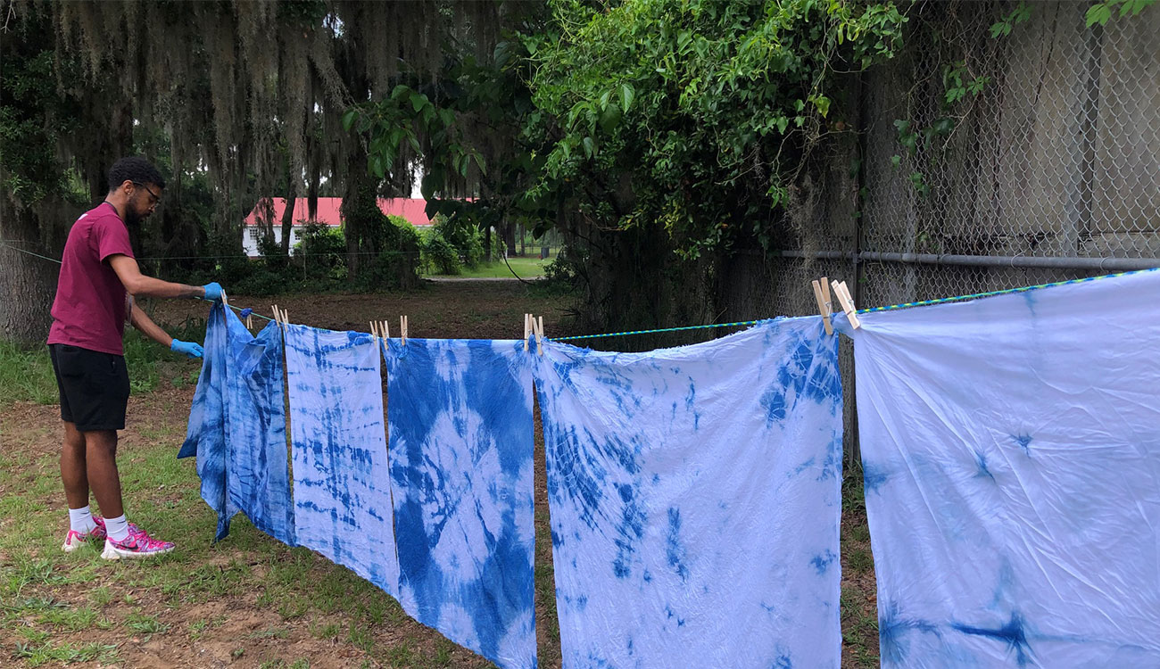 Cameron Nesmith hangs his indigo-dyed fabric with others on a clothesline outside the Emory Campbell Dining Hall at Penn Center.