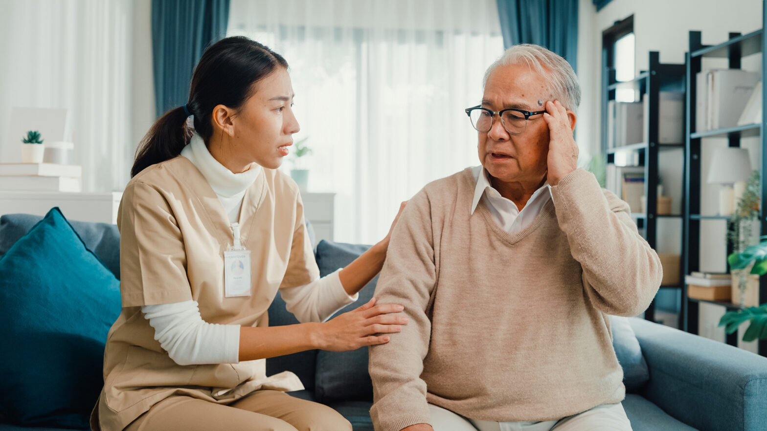 Young Asian female professional caregiver take care touch to calm sick elderly male patient in living room at home. Girl personal care support mature man patient in nursing house, Healthcare.