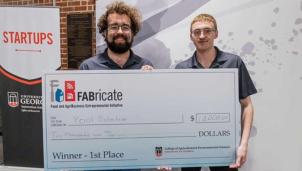 Uga College of Engineering Students Garret Stigall and Guy Gober holding a large check for their Pool Protection pitch.
