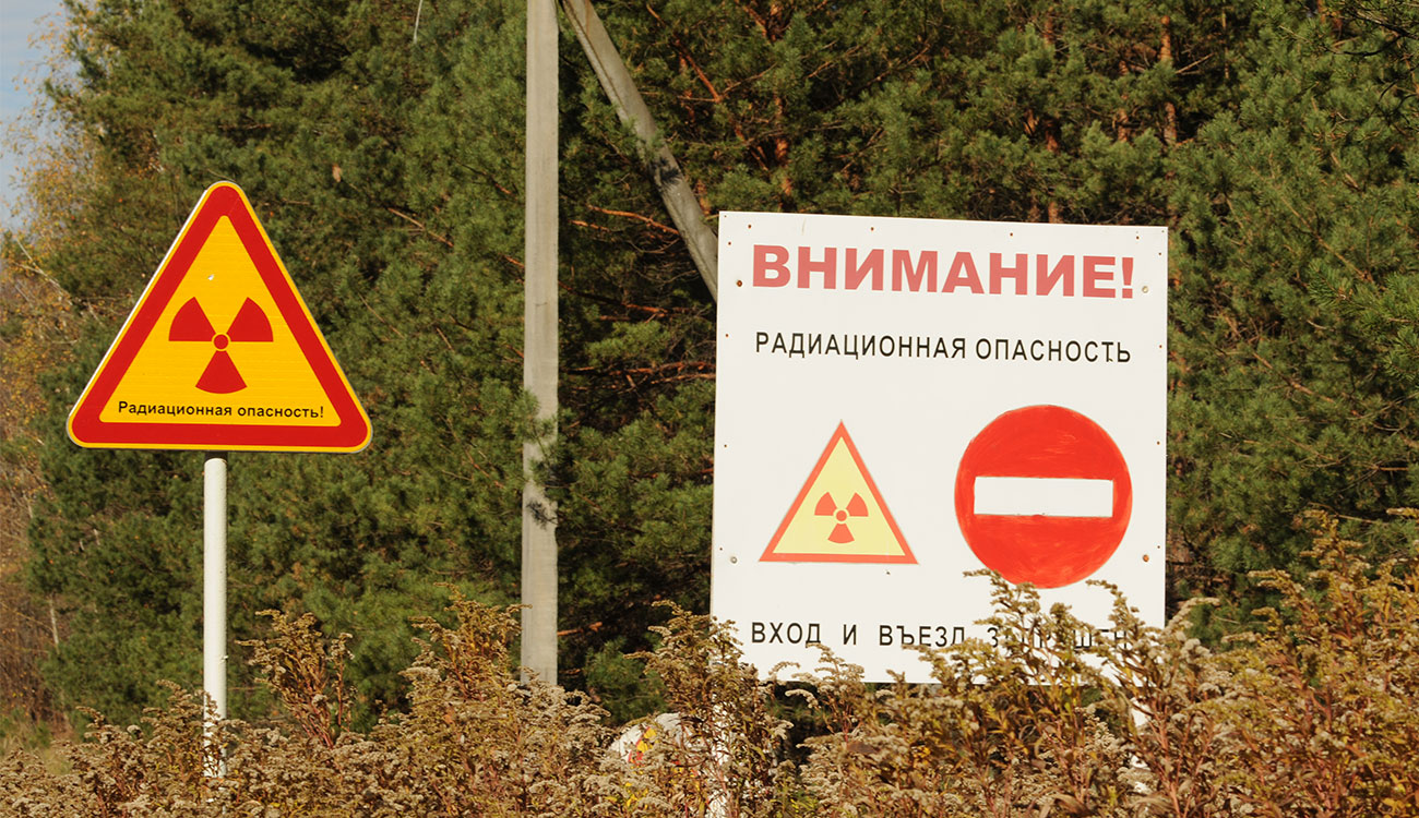 Two signs sit outside the Chernobyl Exclusion Zone. The sign on the right translates to "Attention! Radiation Hazzard" and the sign on the left reads "Radiation danger!"