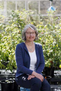 Esther van der Knaap, smiling, poses for a photo inside a greenhouse.