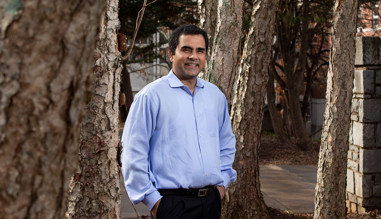 Puneet Dwivedi poses among trees in a light blue shirt and black pants.