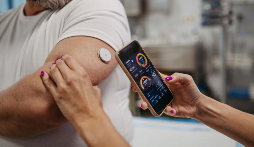 A Woman monitoring a patient's blood sugar levels with a device on the patient's arm and a phone