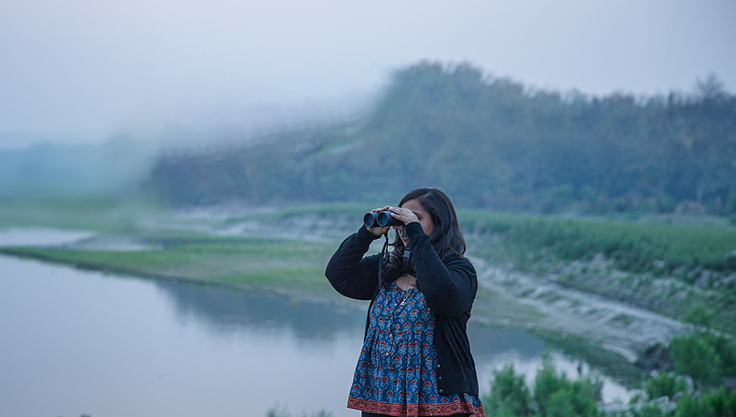 Researcher using binoculars to survey a river.