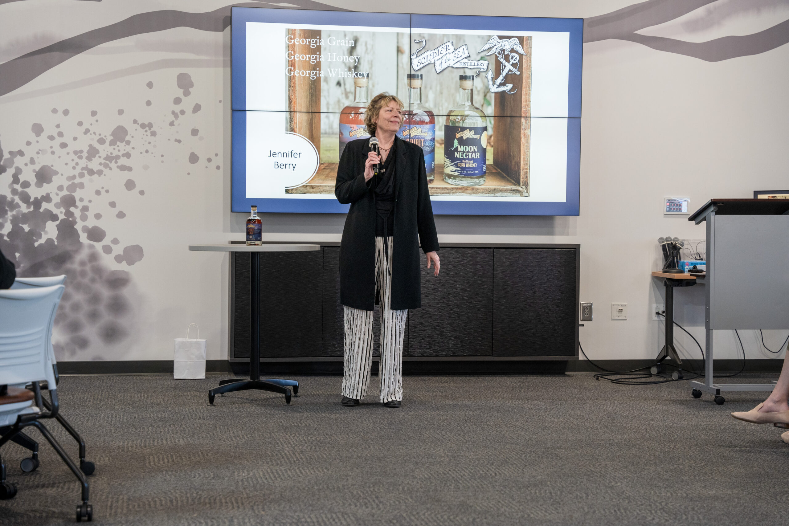 Woman standing holding a microphone in front of a class.