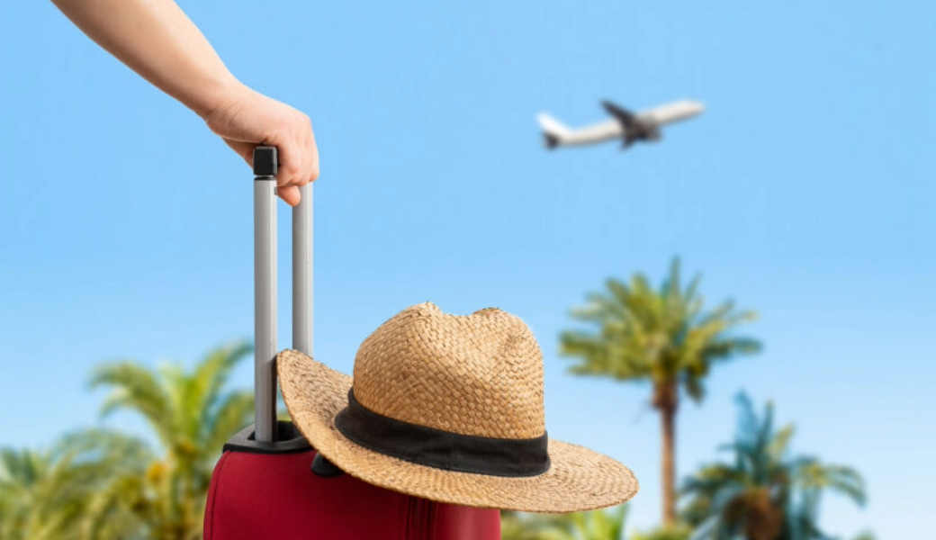 image of a suitcase with a sunhat on top and a background with palm trees and an airplane