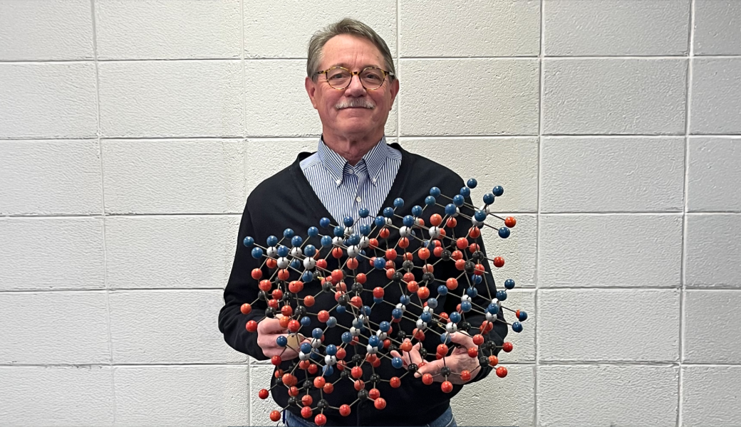 Photo of UGA professor of geology Paul Schroeder holding a crystal model of the mineral kaolinite.