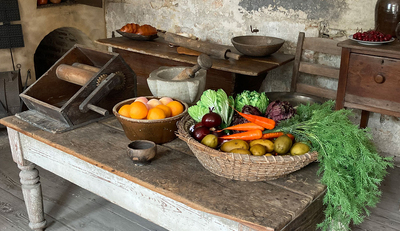 Baskets of fake vegetables, a mortar and pestle, and other common colonial kitchen appliances sit on a table in an exhibit at the Heyward Washington House.