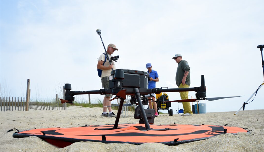 Claudia Venherm (center), Mike Robinson (left) and Kyle Krezdorn prepare to fly a LiDAR drone on Tybee Island in April 2025. (Photo by Jackson K. Schroeder)