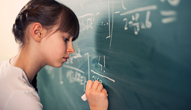 Girl writing out a math problem on a classroom chalkboard.