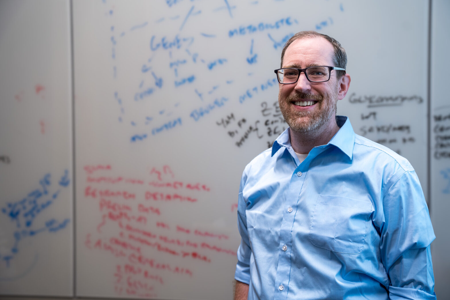 Nathan Lewis in front of a whiteboard with formulas written on it.