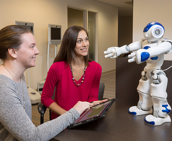 Graduate student Kasey Smith and professor Jenay M. Beer look at interactive companion robots in the Beers laboratory