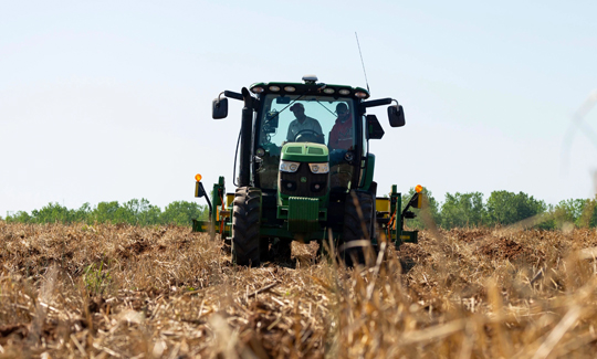 Farmer on a green John Deere tractor harvesting a field.